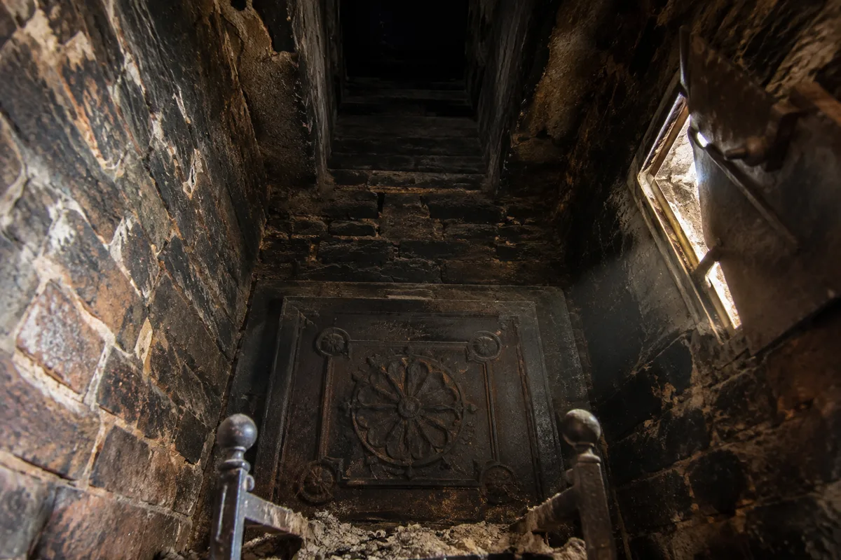 Conduit de cheminée vu depuis le foyer, plaque de fonte ancienne et trappe de ramonage ouverte