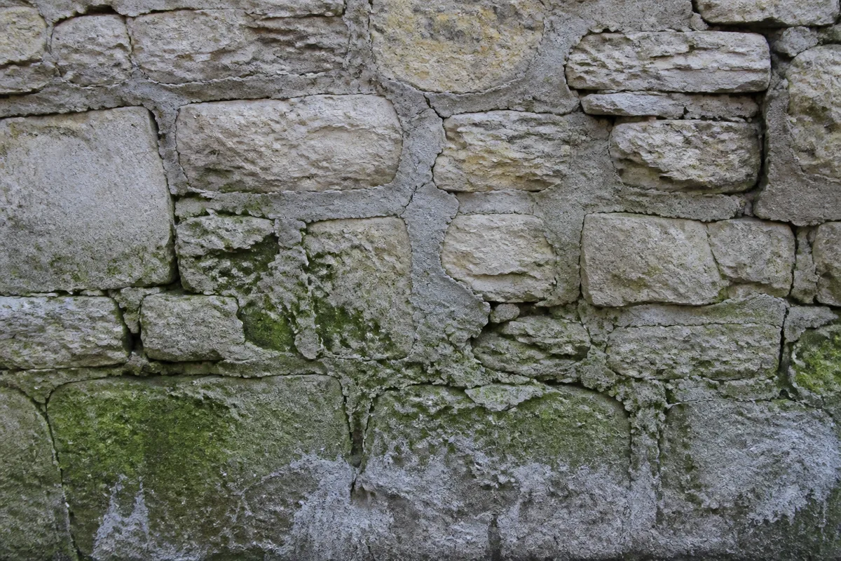 Mur en pierre dégradé montrant des joints au ciment fissurés et des pierres délitées par le gel