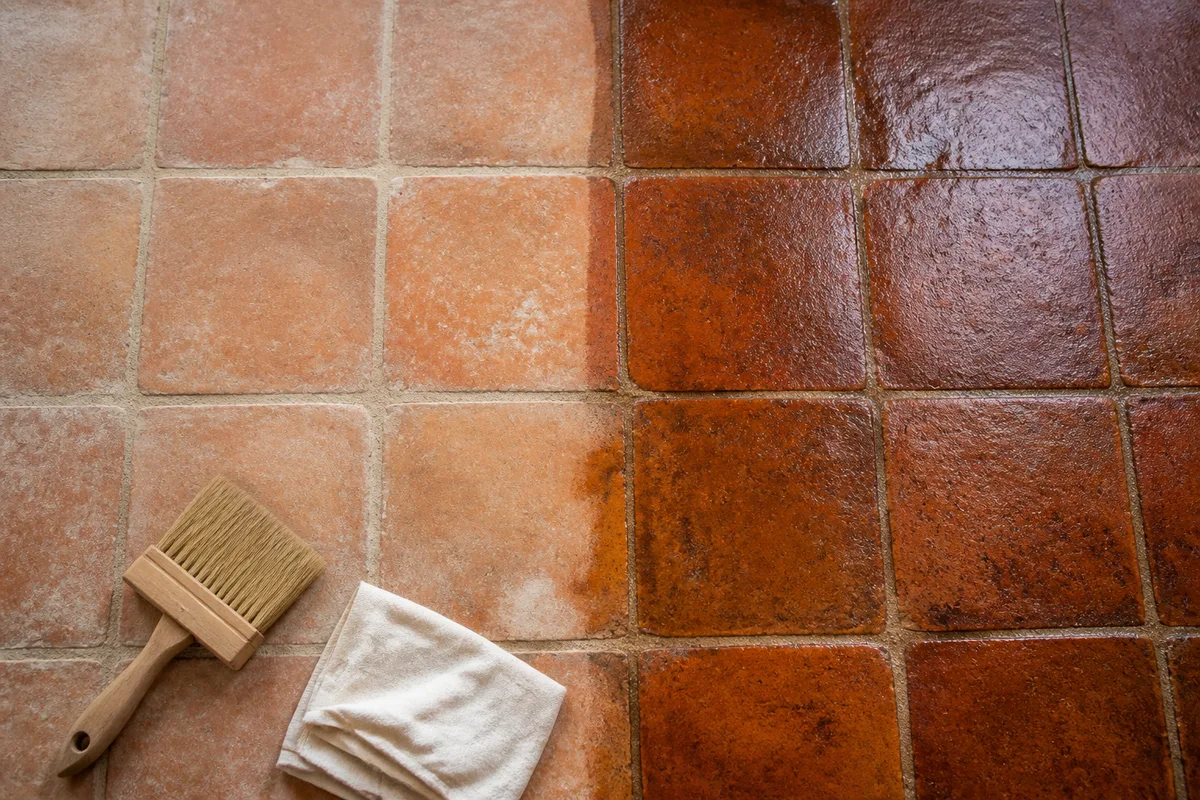 Carreaux de terre cuite fraîchement huilés au rendu mat satiné, pinceau posé au sol, lumière naturelle douce