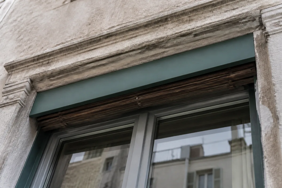 Détail d’un lambrequin en tôle peinte masquant un coffre au-dessus d’une baie ancienne